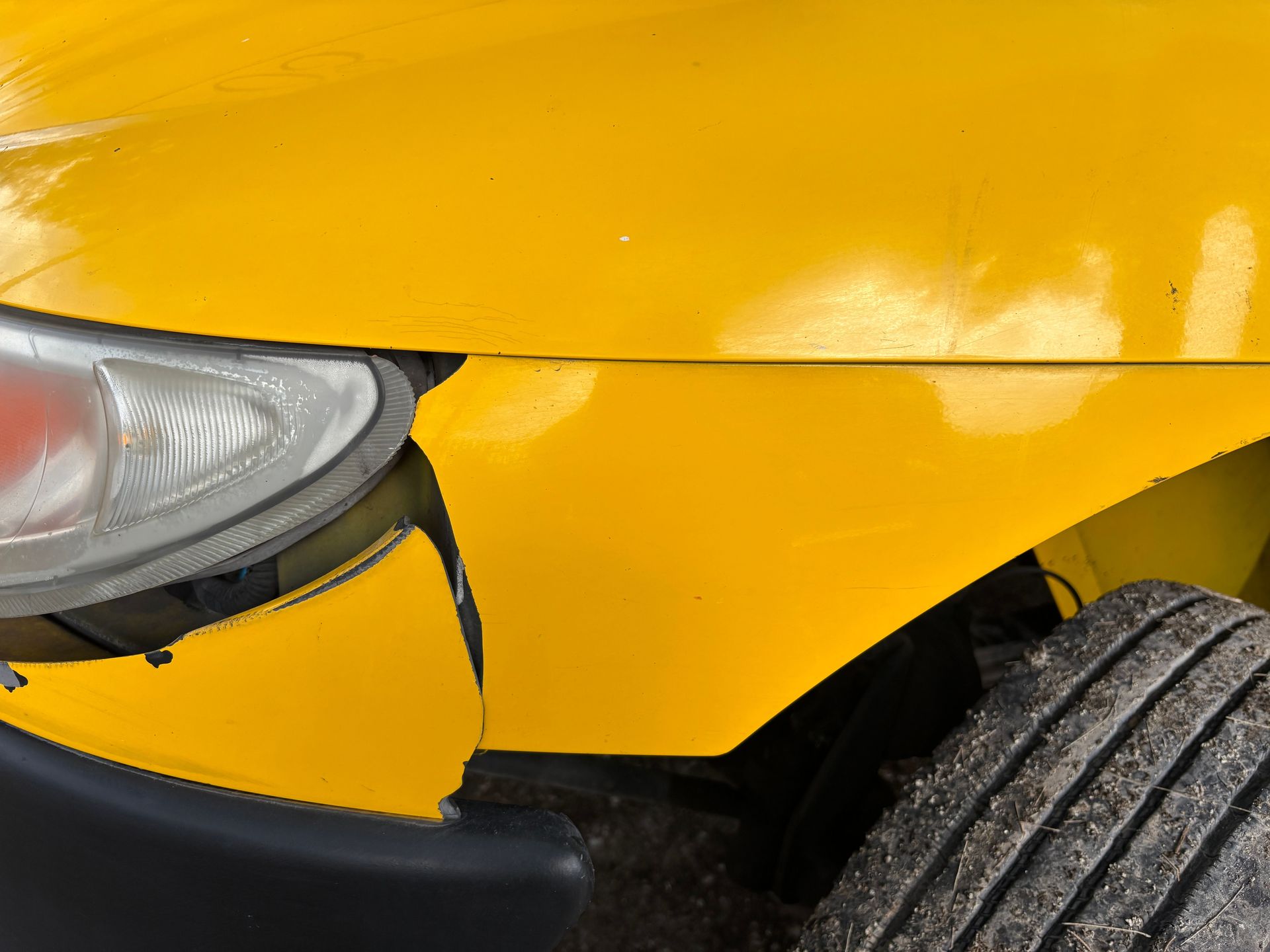 Close-up image of a yellow car's damaged front bumper and headlight for insurance or accident concept.