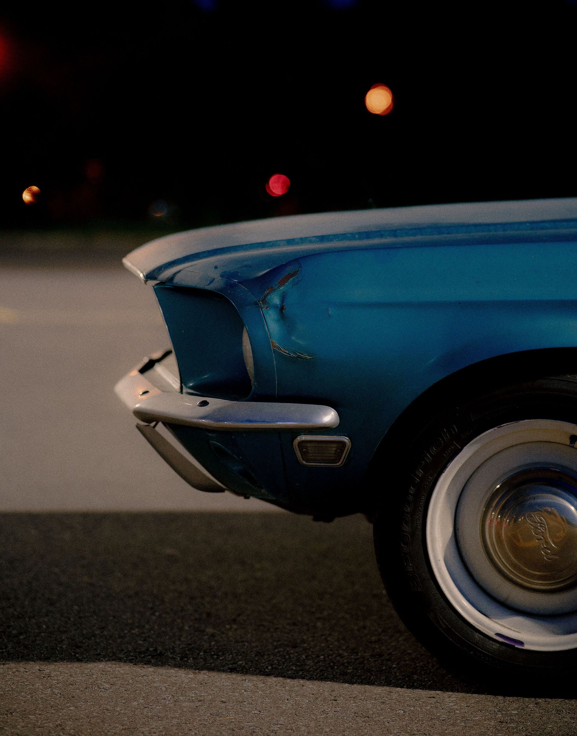 Close-up of a classic blue car with visible dents at night, showcasing vintage design and wear.