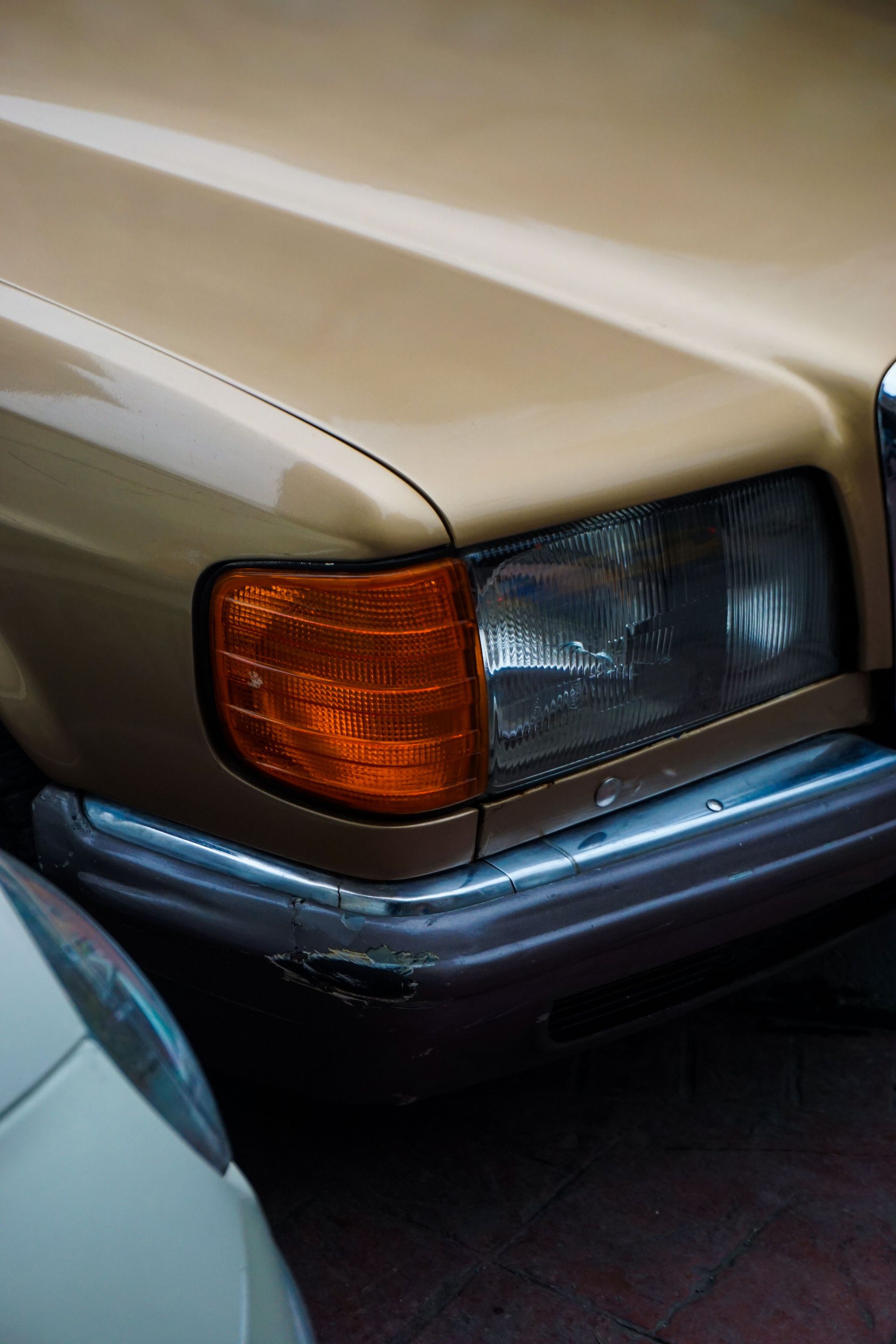 Close-up of a vintage Mercedes headlight in a yellow tone, showcasing classic car design.
